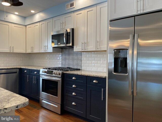 kitchen featuring appliances with stainless steel finishes, dark wood-type flooring, white cabinetry, blue cabinetry, and light stone counters