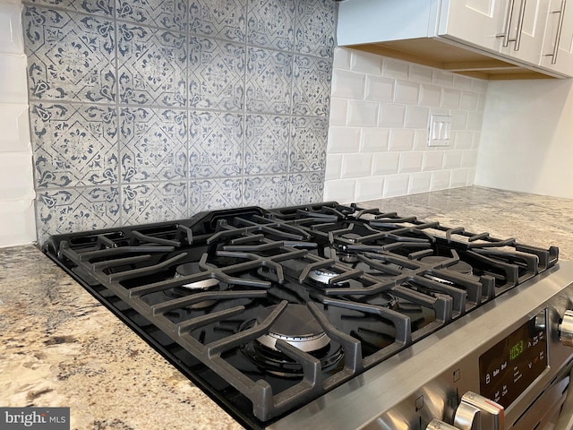 interior details featuring white cabinetry, light stone countertops, backsplash, and cooktop