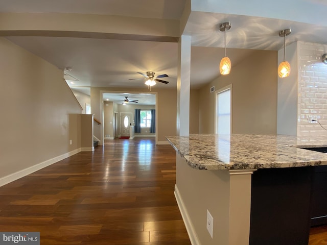 kitchen with kitchen peninsula, ceiling fan, dark hardwood / wood-style flooring, pendant lighting, and light stone counters