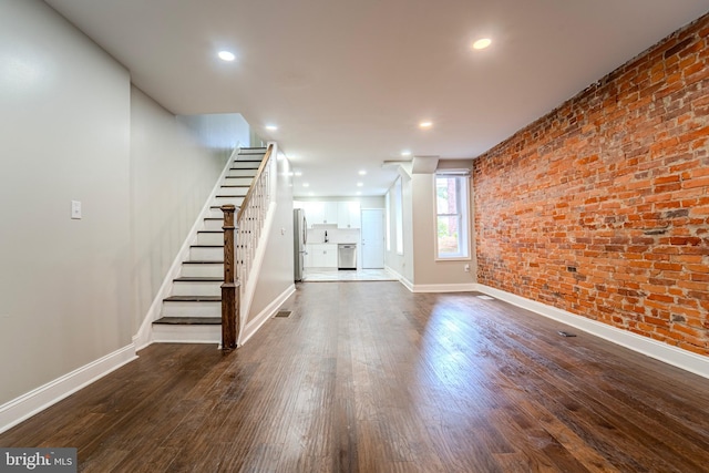 unfurnished living room with brick wall and dark hardwood / wood-style flooring