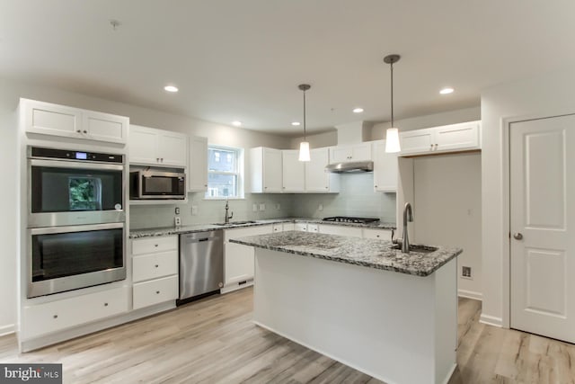 kitchen with white cabinetry, appliances with stainless steel finishes, hanging light fixtures, light stone countertops, and a kitchen island