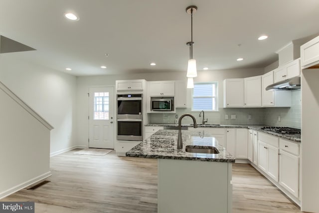 kitchen featuring pendant lighting, appliances with stainless steel finishes, an island with sink, white cabinets, and dark stone counters