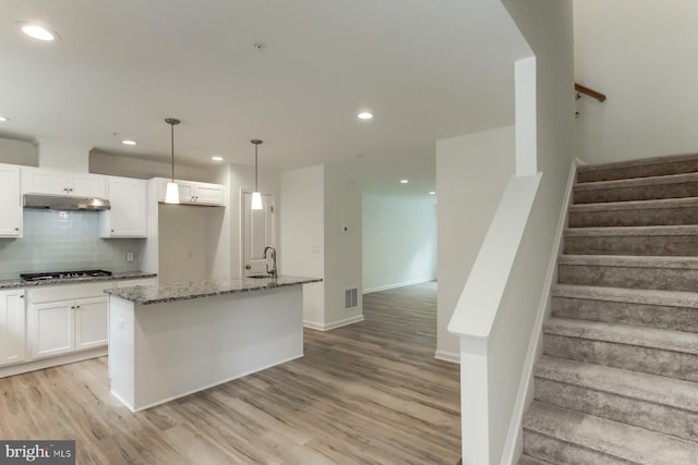 kitchen with pendant lighting, white cabinetry, stainless steel gas cooktop, and an island with sink