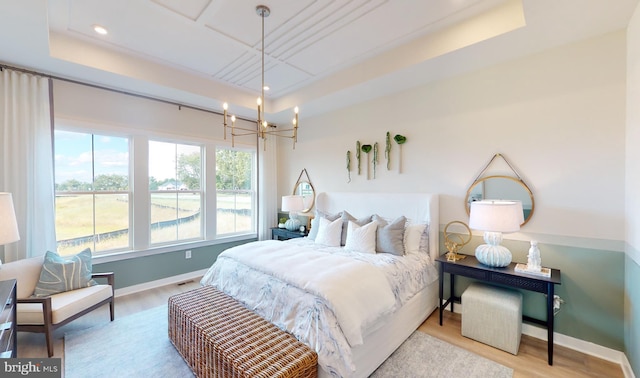 bedroom with a notable chandelier, a tray ceiling, and light hardwood / wood-style floors