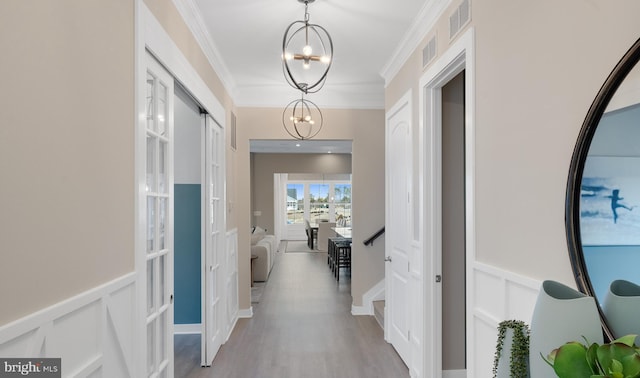 hallway featuring an inviting chandelier, ornamental molding, and light hardwood / wood-style floors