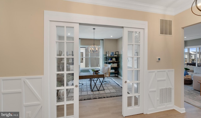 interior space with french doors, a notable chandelier, ornamental molding, and wood-type flooring