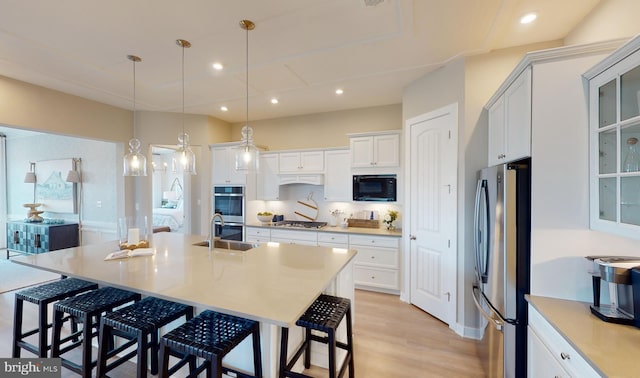 kitchen with hanging light fixtures, a kitchen island with sink, a breakfast bar area, stainless steel appliances, and white cabinets