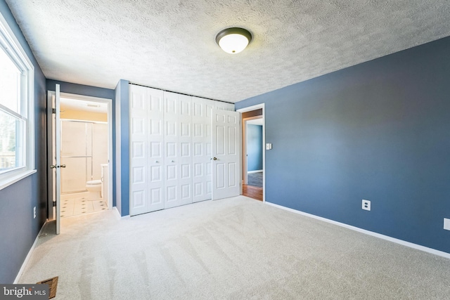 unfurnished bedroom featuring a closet, ensuite bathroom, carpet, and a textured ceiling