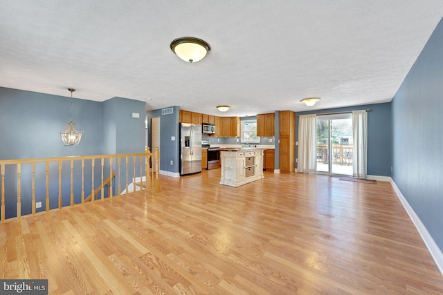 kitchen featuring decorative light fixtures, a center island, light hardwood / wood-style floors, stainless steel appliances, and a textured ceiling