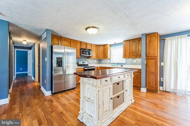 kitchen featuring sink, light hardwood / wood-style flooring, appliances with stainless steel finishes, a center island, and a textured ceiling