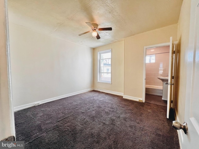 unfurnished bedroom featuring ceiling fan, ensuite bathroom, a textured ceiling, and dark colored carpet