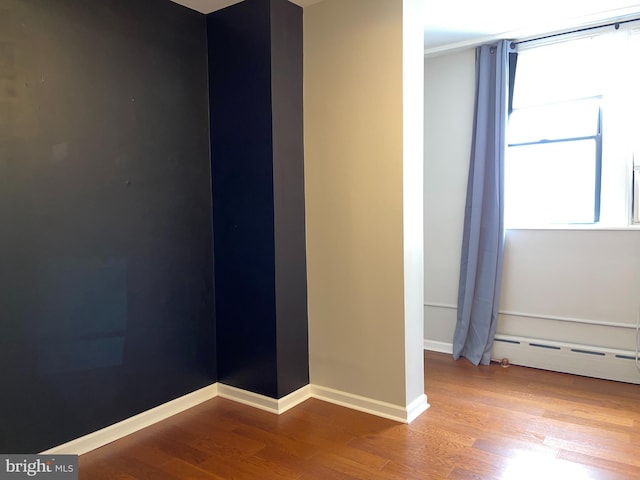 unfurnished room with a baseboard heating unit and wood-type flooring