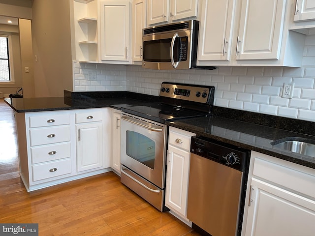 kitchen featuring appliances with stainless steel finishes, white cabinetry, tasteful backsplash, light hardwood / wood-style floors, and dark stone counters