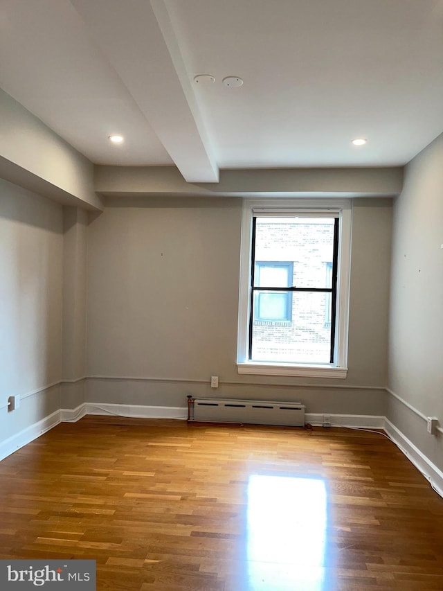 unfurnished room featuring beamed ceiling, a baseboard radiator, and light hardwood / wood-style floors