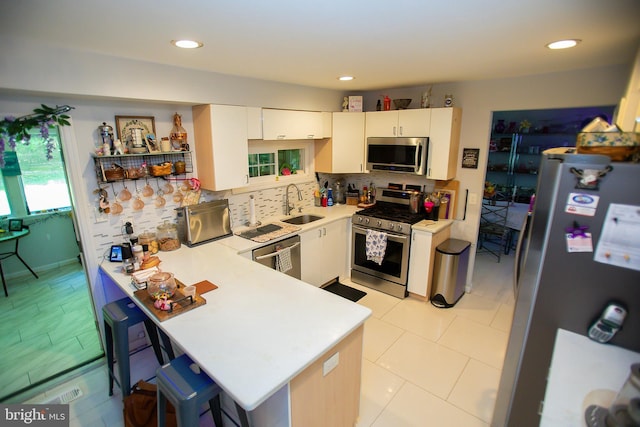 kitchen with sink, white cabinetry, stainless steel appliances, a kitchen bar, and kitchen peninsula