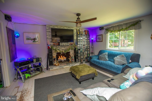 living room featuring wood-type flooring, a stone fireplace, and ceiling fan