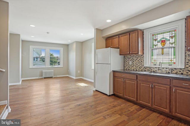 kitchen featuring radiator, white fridge, decorative backsplash, sink, and light hardwood / wood-style flooring