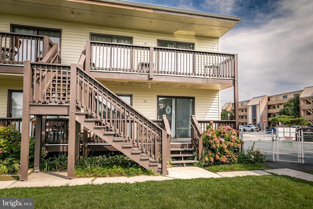 rear view of property with a balcony, stairs, and fence