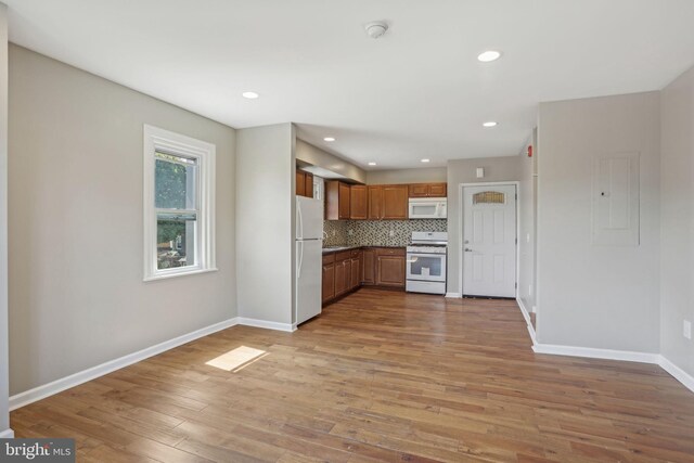 kitchen with light wood-type flooring, white appliances, and decorative backsplash