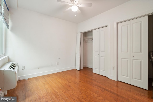 unfurnished bedroom featuring ceiling fan, hardwood / wood-style flooring, and multiple closets