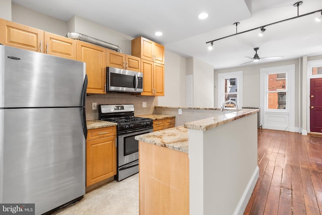 kitchen with ceiling fan, stainless steel appliances, rail lighting, light wood-type flooring, and light stone countertops