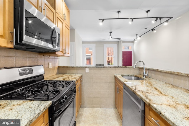 kitchen with appliances with stainless steel finishes, sink, light stone counters, rail lighting, and ceiling fan