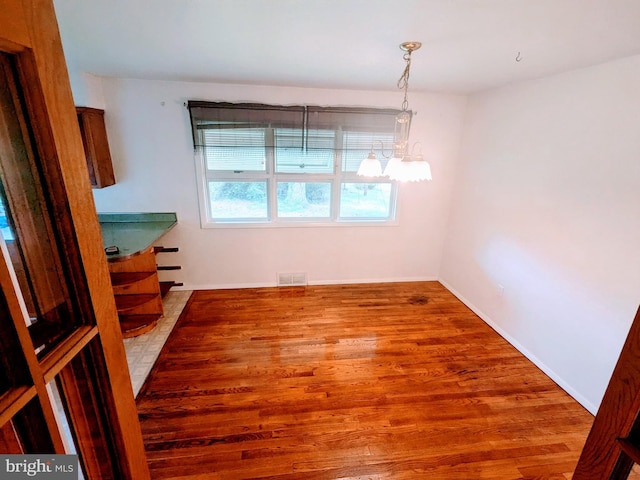 unfurnished dining area with an inviting chandelier and hardwood / wood-style flooring