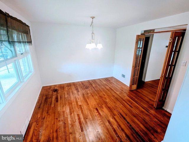 unfurnished bedroom with a notable chandelier and wood-type flooring