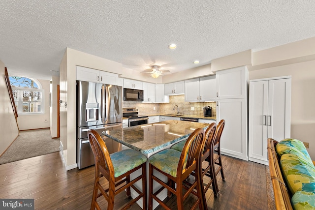 kitchen featuring dark stone counters, white cabinets, dark carpet, appliances with stainless steel finishes, and a kitchen breakfast bar