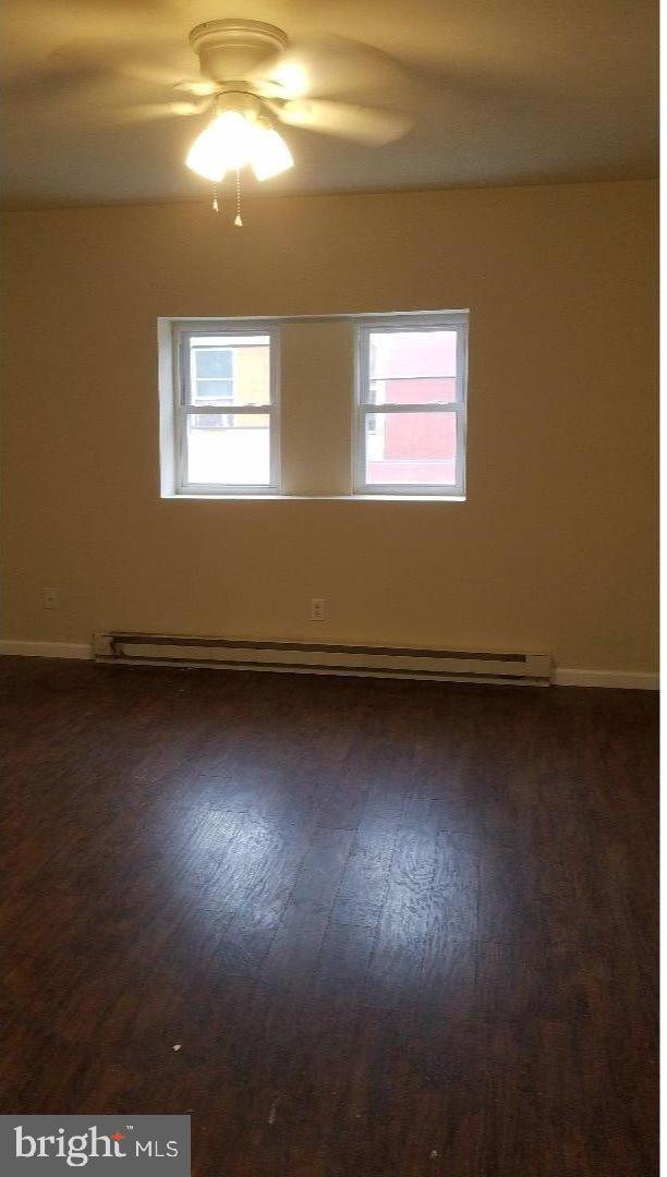 spare room with a baseboard heating unit, dark wood-type flooring, and ceiling fan