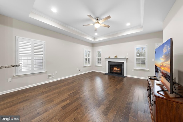 living room with ceiling fan, dark wood-type flooring, a tray ceiling, and ornamental molding