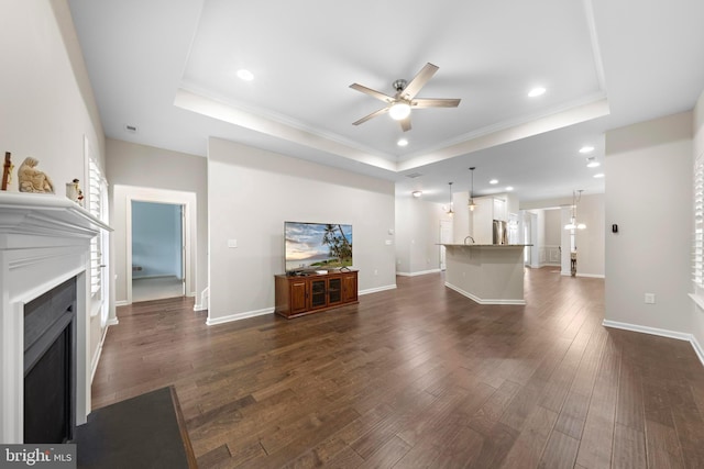 unfurnished living room with ceiling fan with notable chandelier, ornamental molding, dark wood-type flooring, and a tray ceiling