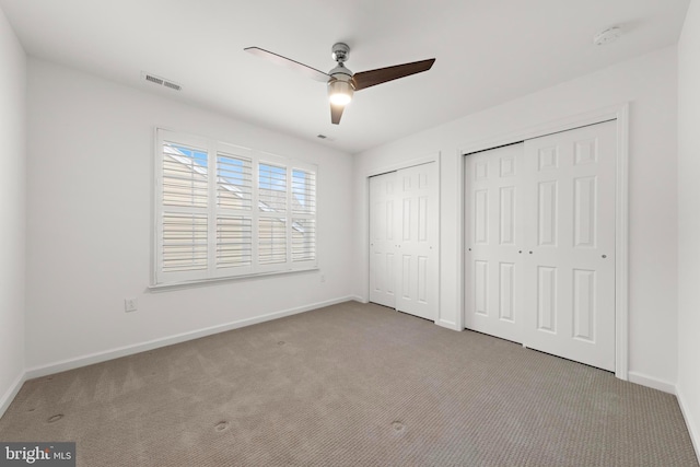 unfurnished bedroom with light colored carpet, two closets, and ceiling fan