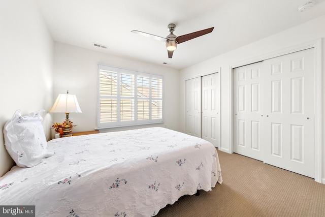 bedroom featuring ceiling fan, light carpet, and two closets