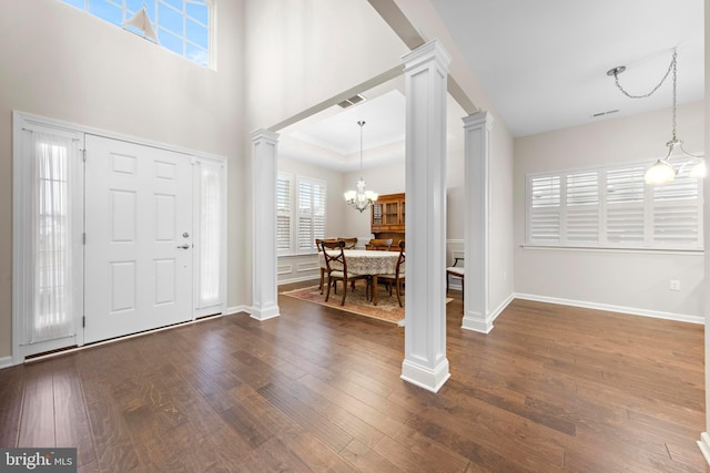 foyer entrance with decorative columns, dark wood-type flooring, a tray ceiling, and a chandelier