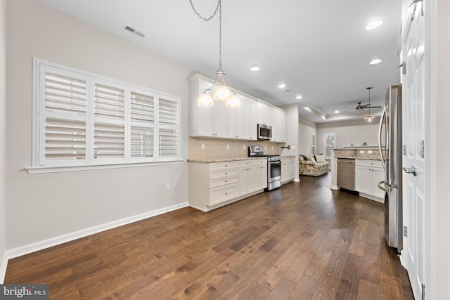 kitchen featuring pendant lighting, dark hardwood / wood-style flooring, appliances with stainless steel finishes, white cabinets, and light stone countertops