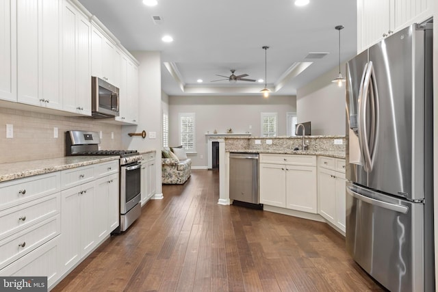 kitchen with light stone counters, pendant lighting, appliances with stainless steel finishes, and a raised ceiling