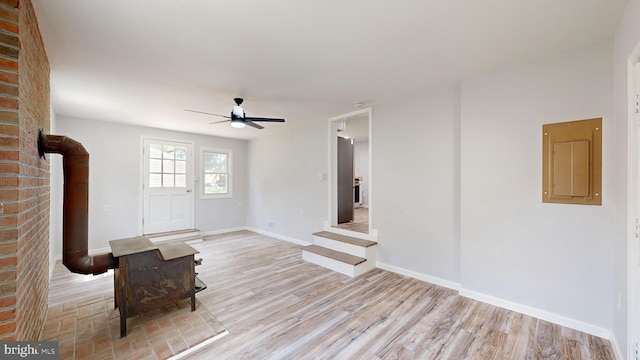 unfurnished living room with ceiling fan, a wood stove, and light hardwood / wood-style flooring