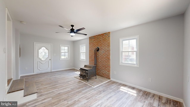 entrance foyer with ceiling fan, a wood stove, and light wood-type flooring