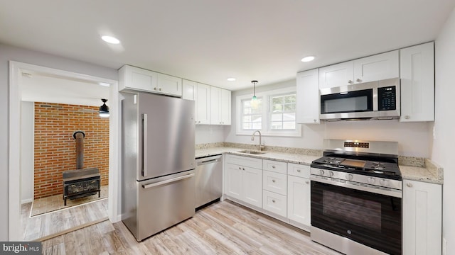 kitchen with white cabinets, appliances with stainless steel finishes, a wood stove, and sink