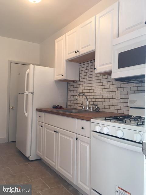 kitchen with white cabinets, dark tile patterned floors, decorative backsplash, and white appliances