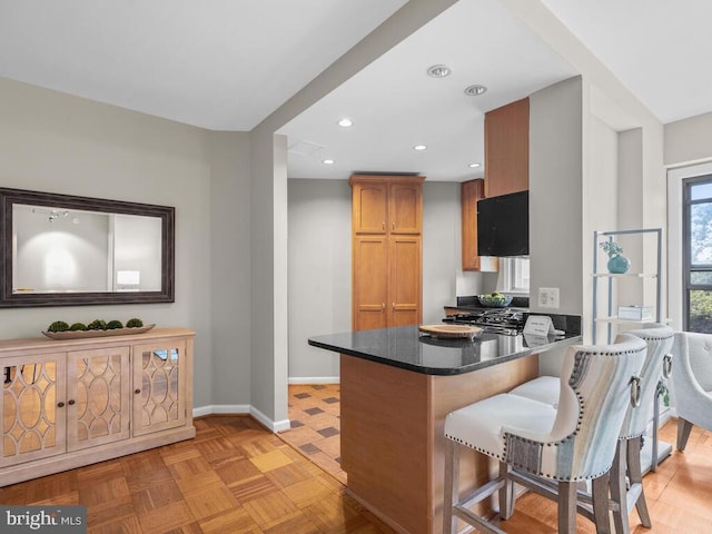 kitchen with a kitchen bar, light parquet floors, kitchen peninsula, and dark stone countertops