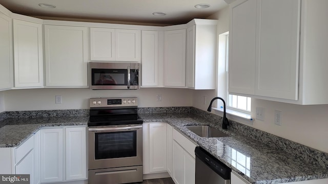 kitchen with dark stone counters, white cabinetry, appliances with stainless steel finishes, and sink