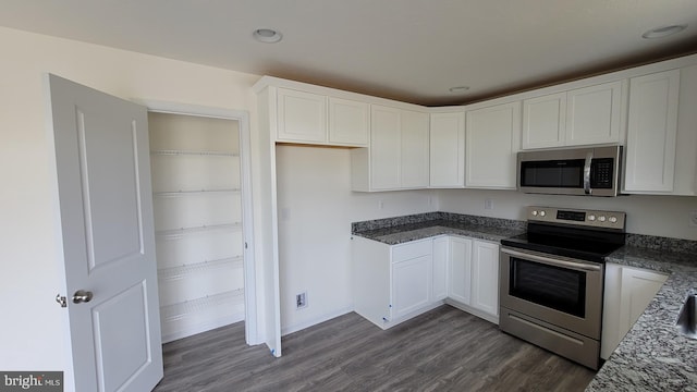 kitchen with white cabinetry, dark wood-type flooring, dark stone countertops, and appliances with stainless steel finishes