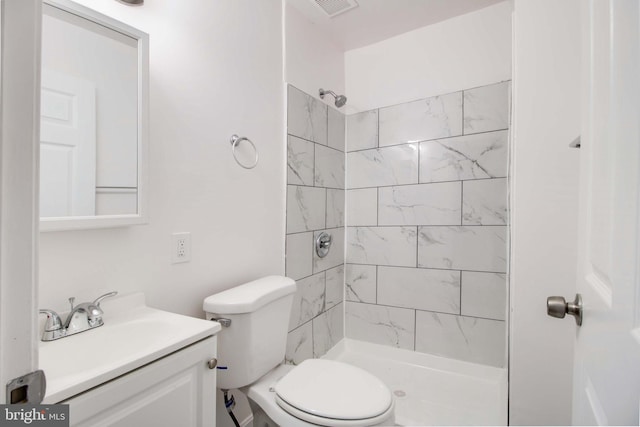 bathroom with toilet, a tile shower, and vanity