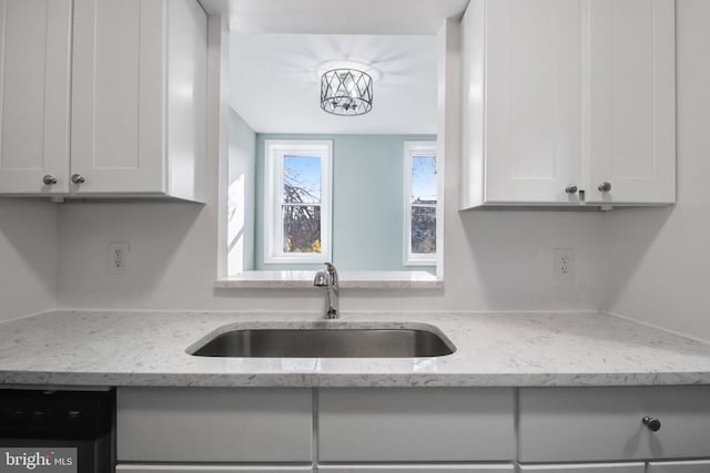 kitchen featuring white cabinetry, black dishwasher, light stone counters, and sink