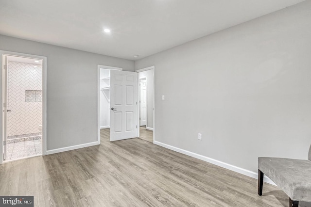 unfurnished bedroom with connected bathroom, a spacious closet, light hardwood / wood-style flooring, and a closet