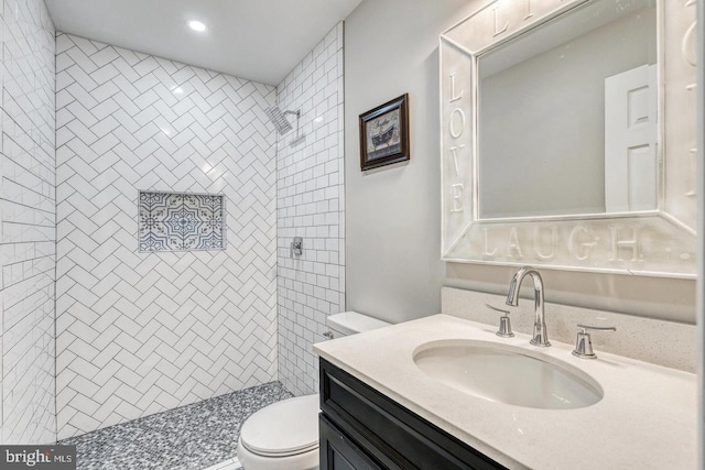 bathroom featuring vanity, a tile shower, and toilet