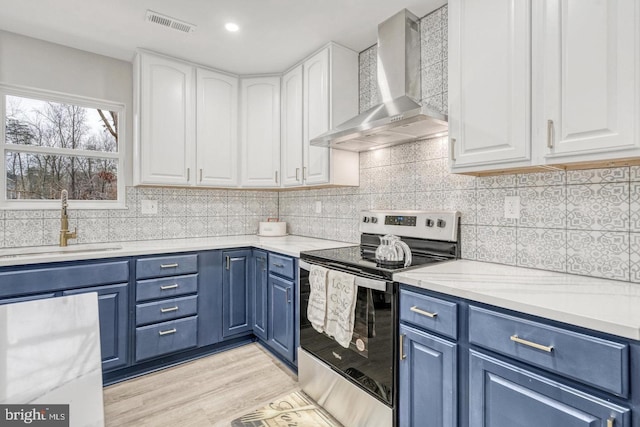 kitchen featuring sink, white cabinets, blue cabinets, stainless steel range with electric cooktop, and wall chimney exhaust hood