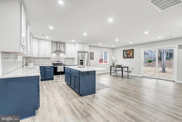 kitchen with a kitchen island, appliances with stainless steel finishes, blue cabinets, white cabinets, and wall chimney exhaust hood